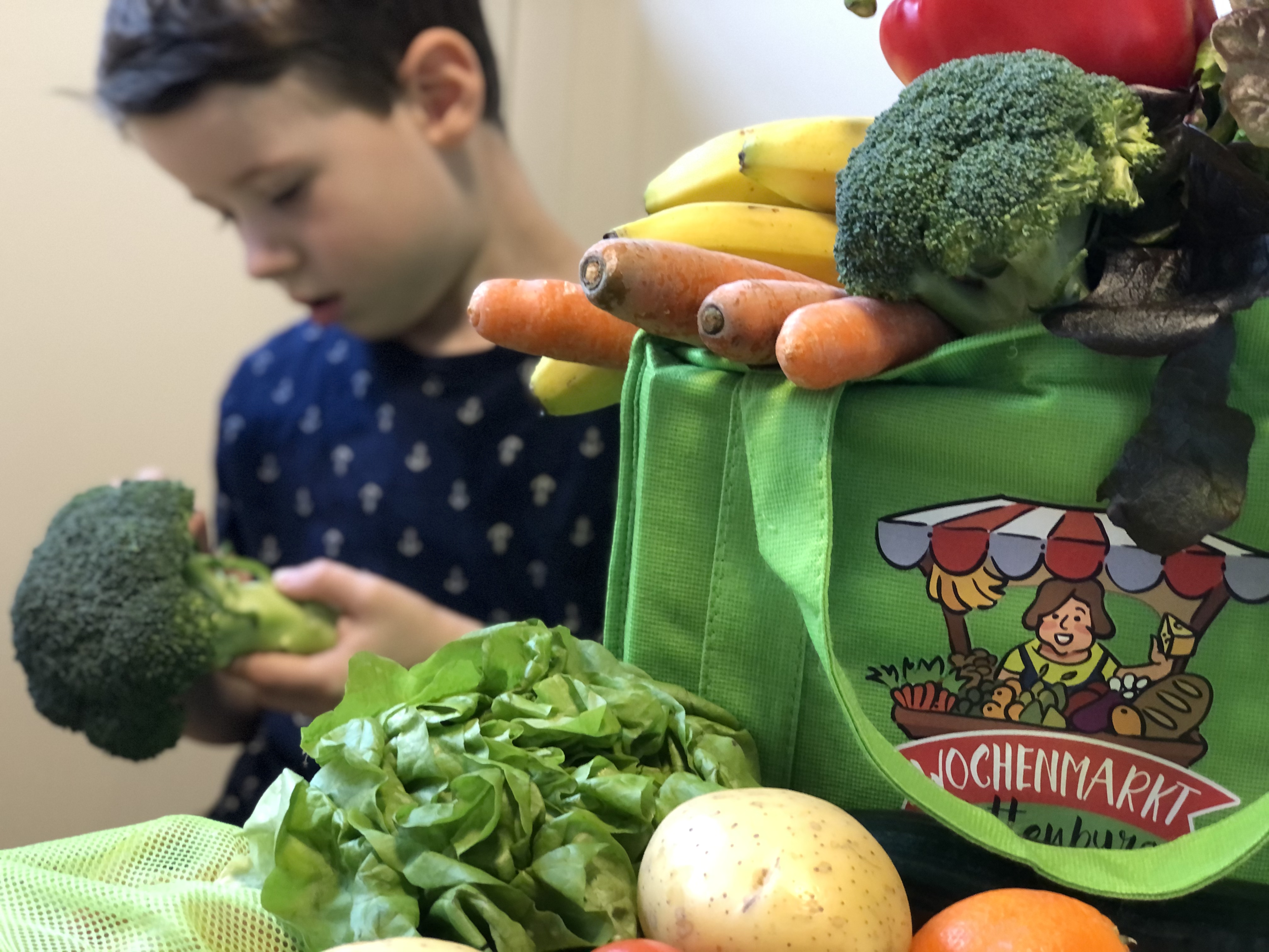 Wochenmarkttasche gefüllt mit Obst und Gemüse und Junge mit Brokkoli