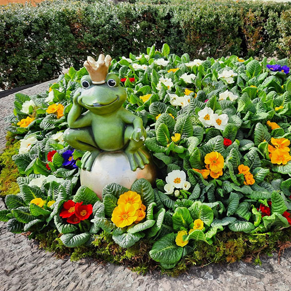 Brunnen gefüllt mit Primeln und dazwischen der Froschkönig