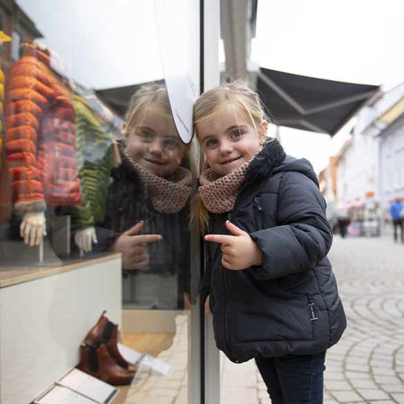 Ein kleines Mädchen steht vor einem Schaufenster und zeigt hinein